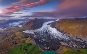 Le glacier Skaftafellsjokull se jette dans un lac glaciaire, entouré de montagnes et de nuages au coucher du soleil dans le sud de l'Islande.