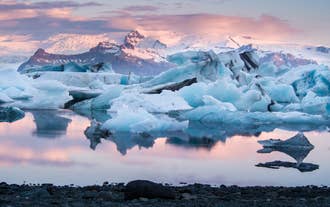 Isbjerge flyder stille ved solnedgang i Jökulsárlón gletsjerlagune, med Vatnajökull-gletsjeren i baggrunden.