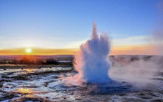 Strokkur Geyser in the Golden Circle of Iceland erupts with boiling water with the midnight sun seen in the distance.