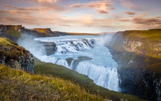 De Gullfoss-waterval in IJsland stort zich in een ravijn onder een pastelkleurige hemel tijdens het gouden uur.