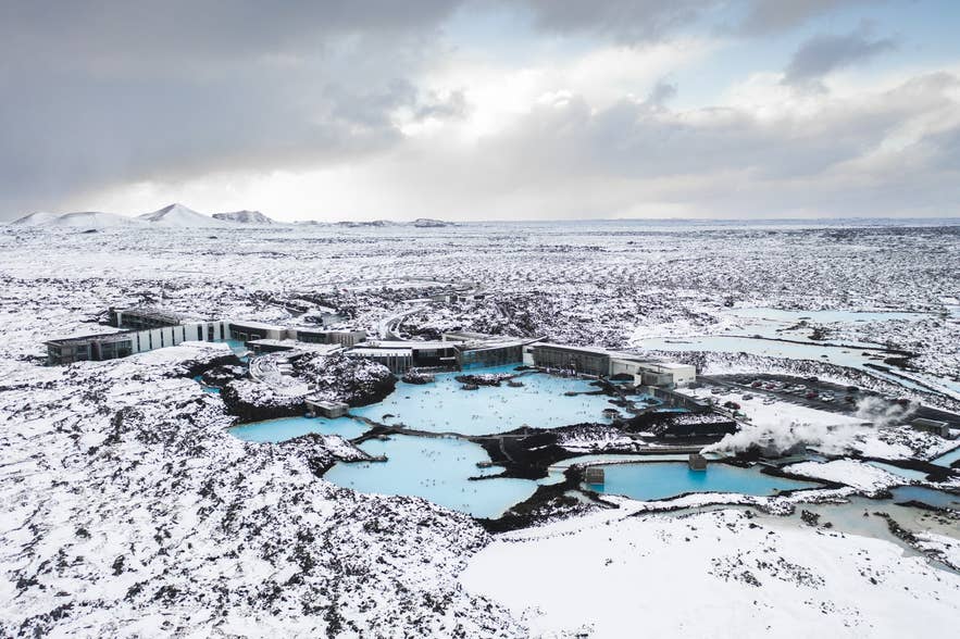 Aerial view of the Blue Lagoon's milky-blue water and spa buildings across a snow-covered lava field