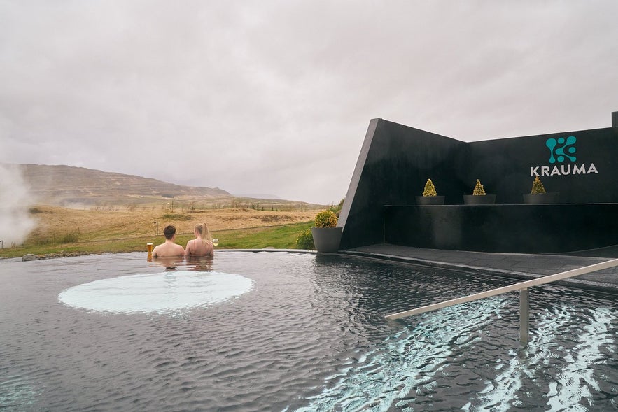 Two people relax in Krauma Spa's hot spring near Borgarnes, with scenic countryside and modern pool design.