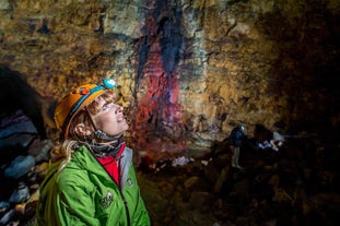 A woman wearing a helmet with a head torch looks around an empty magma chamber on a volcano tour in Iceland.