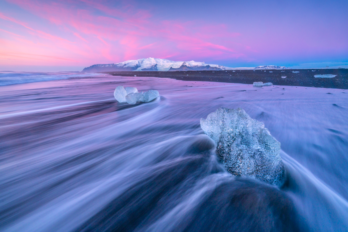 Fascinerande scen vid Diamond Beach, med vågor som flyter mellan isblock under en lila himmel.