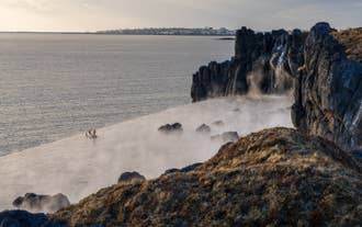 A person bathing at the infinity edge of the Sky Lagoon thermal baths amid misty air and natural surroundings.