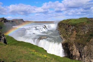 Rainbows appear in the mist at Gullfoss waterfall on a cloudy, blue-sky day..