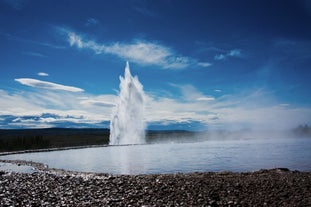 The geyser Strokkur erupts against a vivid blue sky.