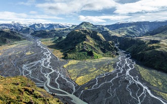 Vista aérea de ríos glaciares trenzados que serpentean entre montañas cubiertas de musgo y terreno volcánico negro en el Valle de Thorsmork.