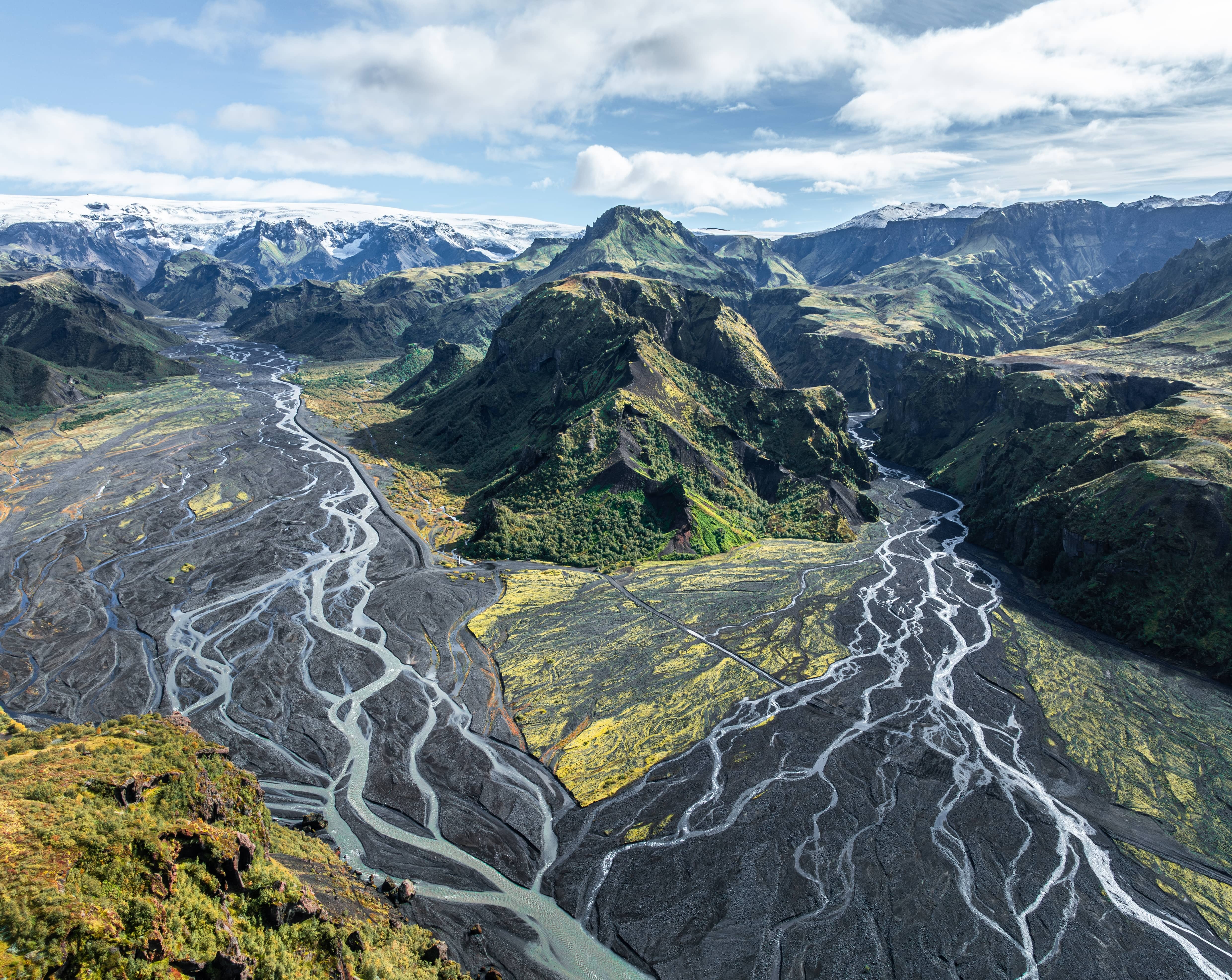 Vue aérienne de rivières glaciaires entrelacées serpentant à travers les montagnes moussues et le terrain volcanique noir de la vallée de Thorsmork, en Islande.