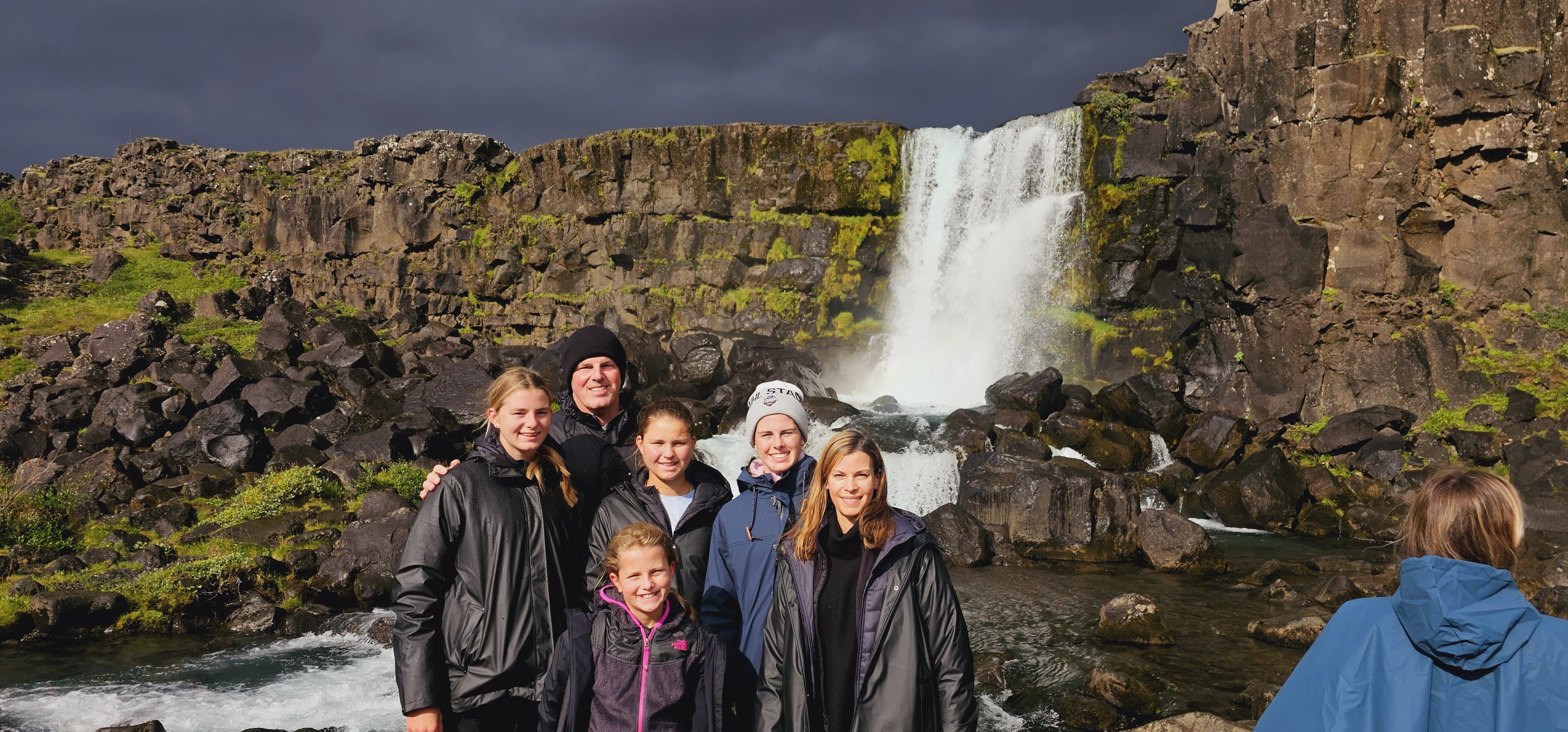 A smiling family poses in front of Oxararfoss Waterfall in Thingvellir National Park, Iceland.