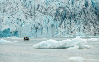 A boat tour approaches the stunning icy wall of Fjallsarlon Glacier Lagoon in South Iceland on a cloudy day.