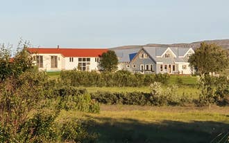 Svanshóll Apartments countryside property with white buildings, red and blue roofs, surrounded by greenery and open fields.