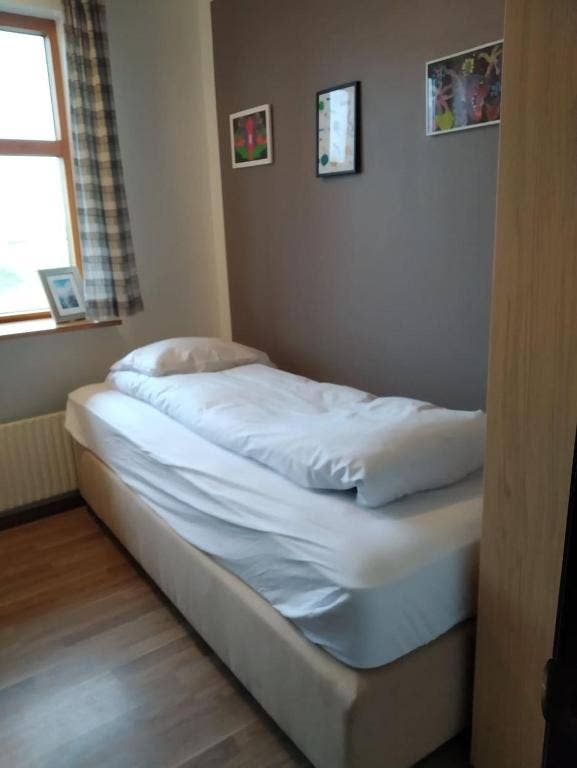 Small guest room with a single bed, wooden floor, framed artwork, and a window with plaid curtains.