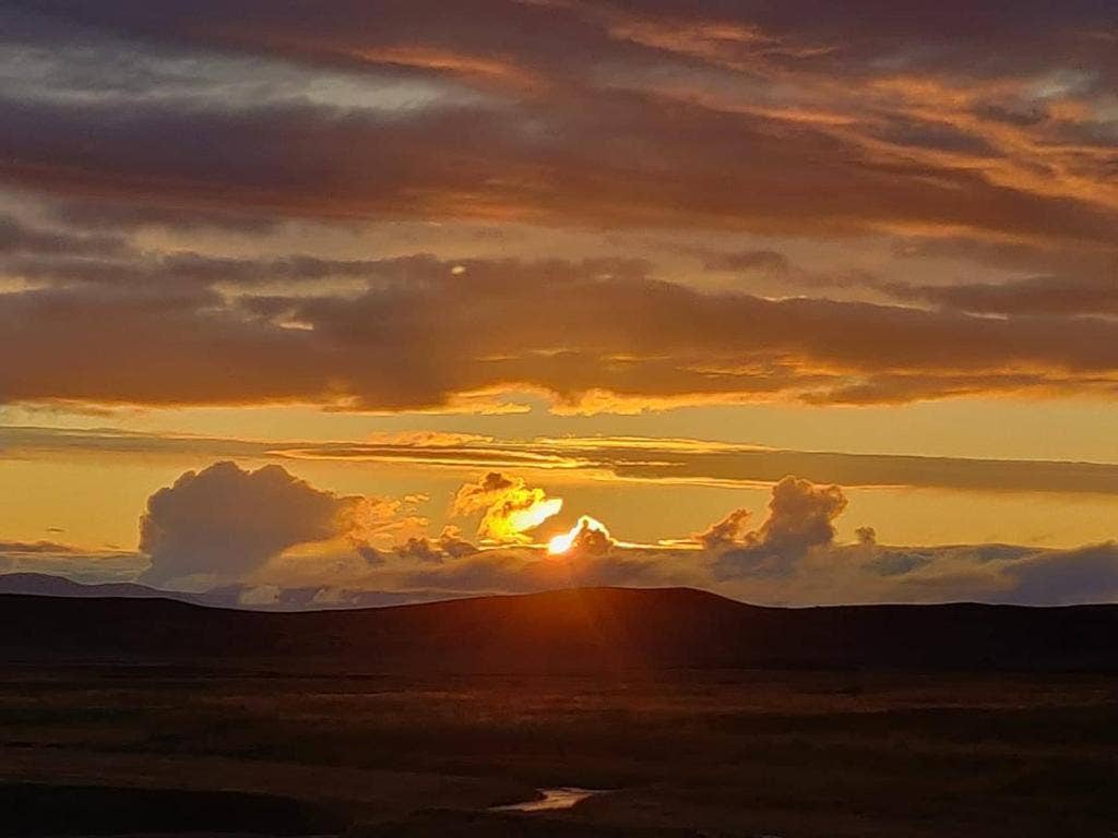 Dramatic sunset over the highlands, with golden light breaking through layered clouds above a dark, rolling landscape.