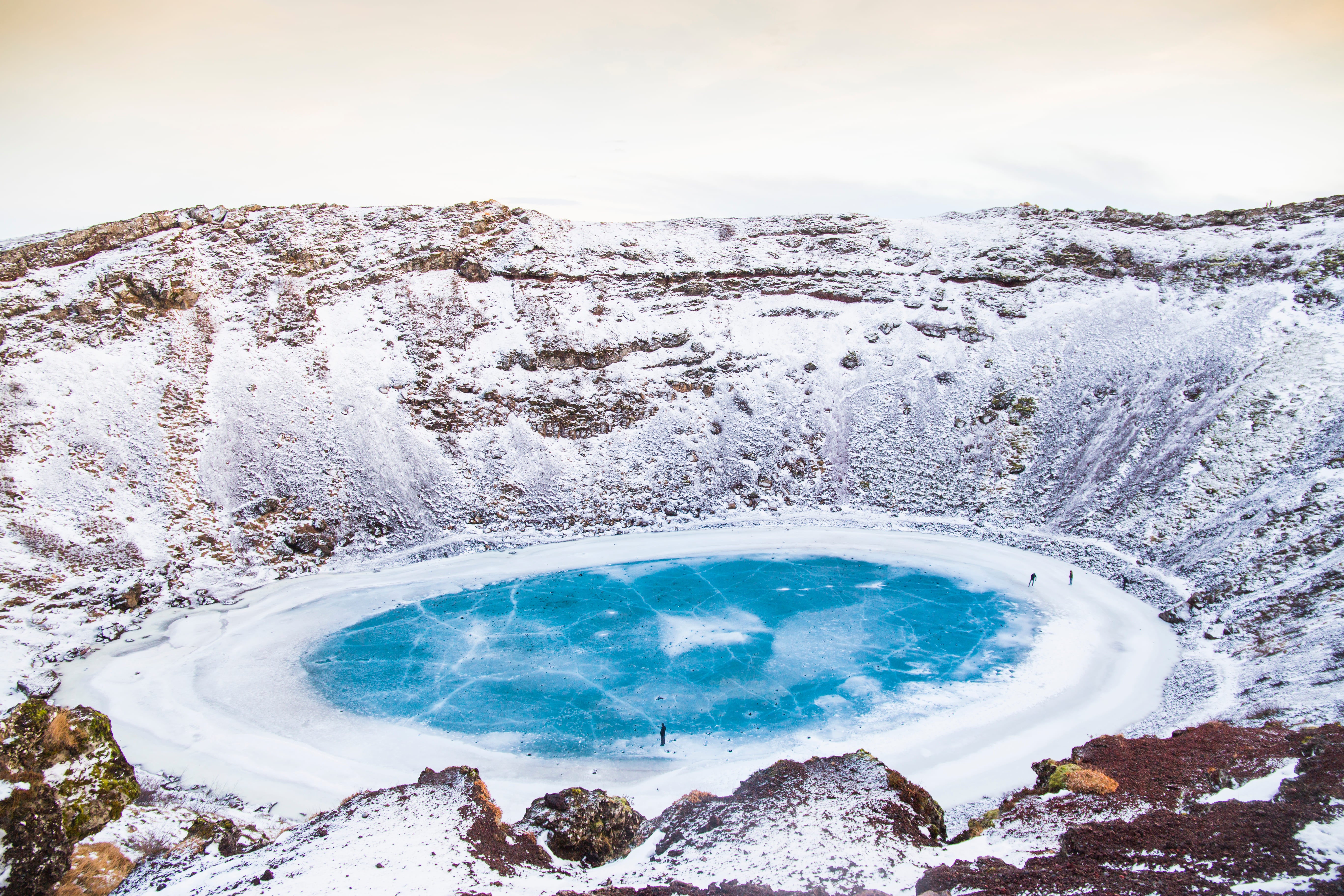 En frossen, blå innsjø i Kerid-krateret på Sør-Island, omgitt av snødekte klipper.