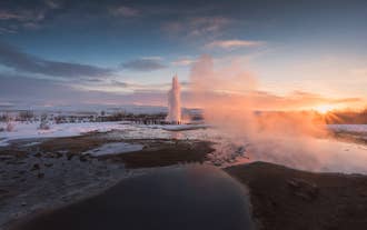 Der Geysir Strokkur bricht bei Sonnenuntergang im geothermischen Gebiet Geysir in Südisland aus.
