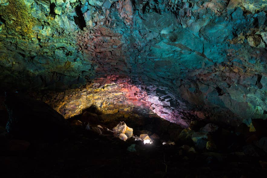 Lit rock walls in shades of green, pink, and yellow inside the Thrihnukagigur magma chamber Lit rock walls in shades of green, pink, and yellow inside the Thrihnukagigur magma chamber