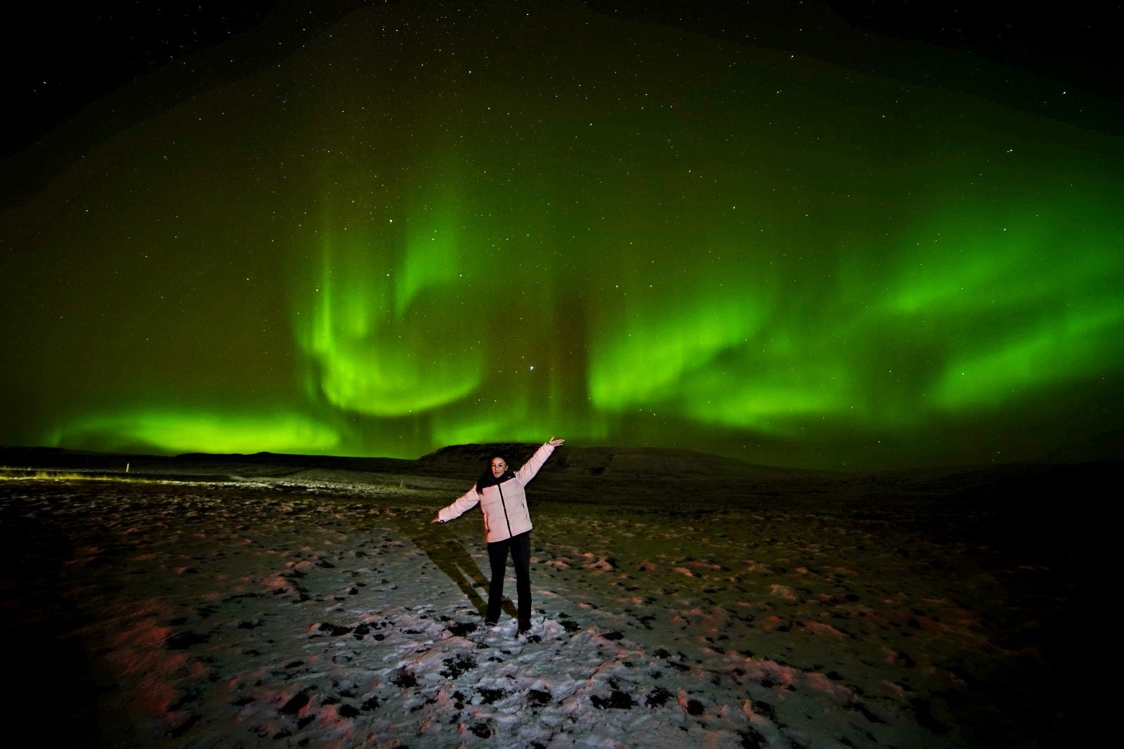 Traveler standing beneath vibrant northern lights on a Reykjavik northern lights tour