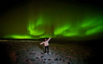 Traveler standing beneath vibrant northern lights on a Reykjavik northern lights tour