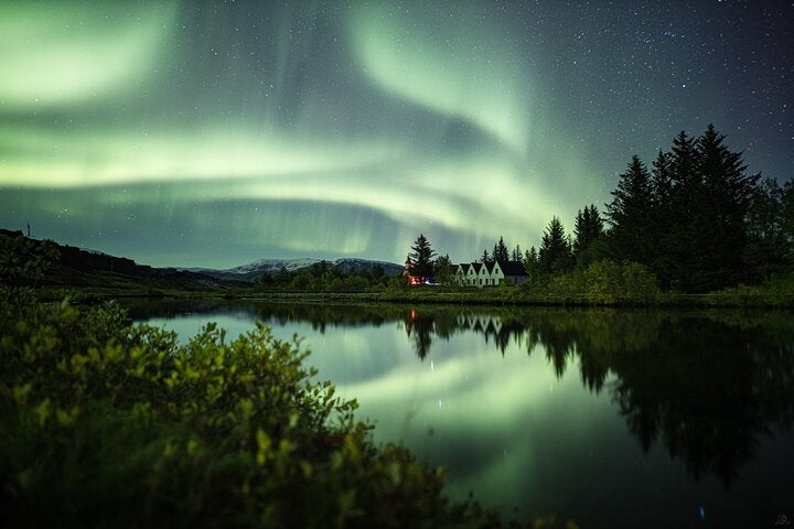 The northern lights above a peaceful lake and a cottage.