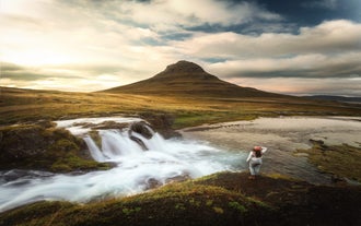Una mujer con gorro de pie ante la montaña Kirkjufell y su cascada.