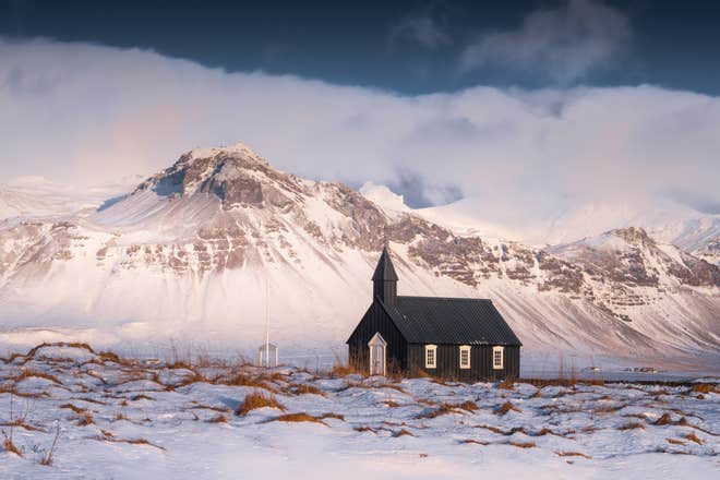 Black Budir Church in snow-covered Snaefellsnes Peninsula with dramatic mountains in the background.t