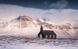 Die schwarze Kirche von Budir auf der verschneiten Halbinsel Snaefellsnes mit einer beeindruckenden Bergkulisse im Hintergrund.