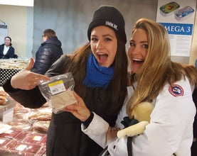 Two women wearing hats. One is pointing at some traditional Icelandic food.