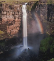 Front view of Haifoss waterfall with a rocky backdrop and a rainbow to the side.