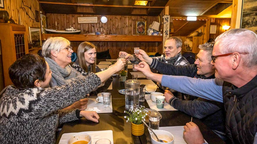 Groep geniet van IJslandse likeur en sterke drank in een gezellig restaurant in Reykjavik, proostend met traditionele schnaps en lokale dranken.