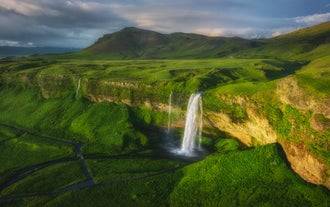 Aerial view of Seljalandsfoss Waterfall cascading from green cliffs into a serene pool on Iceland’s South Coast.
