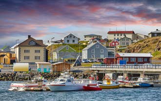 Barcos de pesca atracan en el puerto de Stykkisholmur, Islandia, con casas coloridas bajo un cielo resplandeciente.
