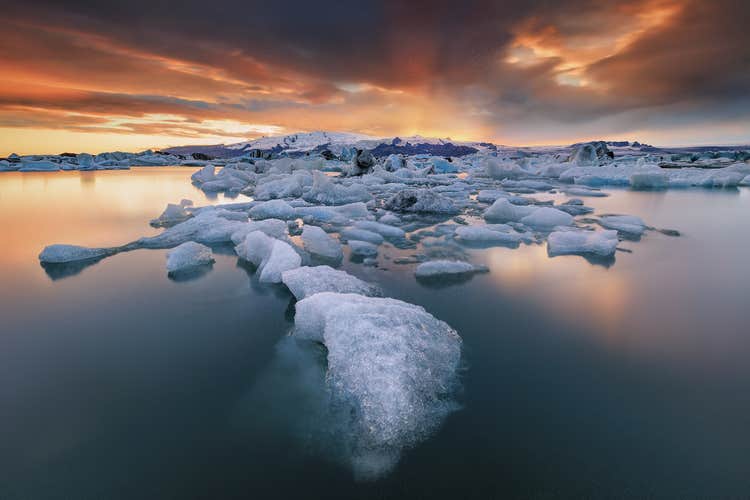 Icebergs floating in Jokulsarlon Glacier Lagoon at sunset, reflecting fiery skies over Iceland's icy landscape.