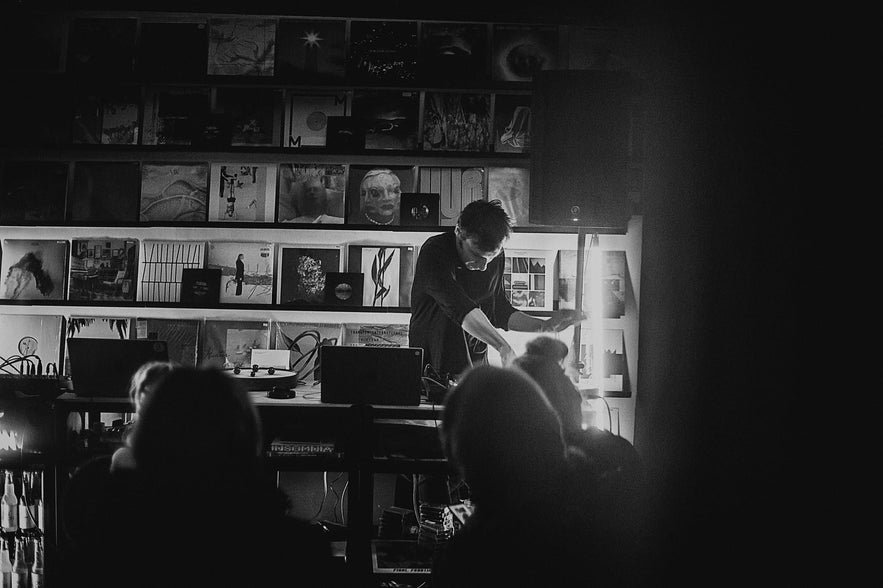 Black and white photo of a live electronic music performance at Space Odyssey in Reykjavík, with vinyl records displayed on the wall behind the artist.