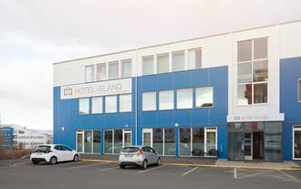 Exterior of Hotel Island Comfort, a modern three-story building with a blue and white facade, large windows, and cars parked in