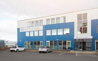Exterior of Hotel Island Comfort, a modern three-story building with a blue and white facade, large windows, and cars parked in 