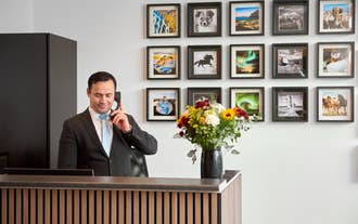 Receptionist in a suit speaking on the phone behind a modern wooden front desk with a vase of fresh flowers, and framed Icelandi