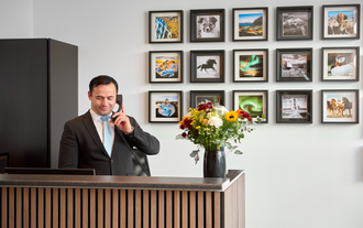 身着西装的前台接待员在现代木质前台接听电话，桌上摆放着新鲜花卉，墙上挂有冰岛风景画。