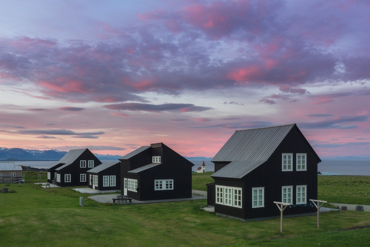 Historische isländische Torfhäuser, eingebettet in eine üppig grüne Wiese unter einem violett-rosa Abendhimmel in Südisland.
