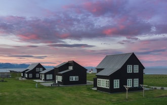 Historiska isländska torvhus inbäddade i ett frodigt grönt fält under en lilarosa kvällshimmel på södra Island.