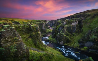El Cañón Fjadrargljufur en el sur de Islandia brilla al atardecer con acantilados cubiertos de musgo, un río serpenteante y cielos coloridos.