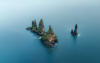 Reynisdrangar sea stacks rise dramatically from the ocean along Iceland’s south coast under a calm summer sky.