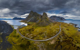 Flygfoto över Eystrahorn och kustvägen på Stokksneshalvön på sydöstra Island under dramatisk himmel.