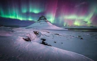 Aurora borealis lyser opp himmelen over fjellet Kirkjufell på Snæfellsnes-halvøya på Island, omgitt av snø og is.