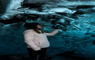 Un visiteur touche la glace bleue de la grotte de glace de cristal