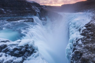 Partially frozen Gullfoss waterfall under a pastel sky in Iceland's snowy winter landscape.