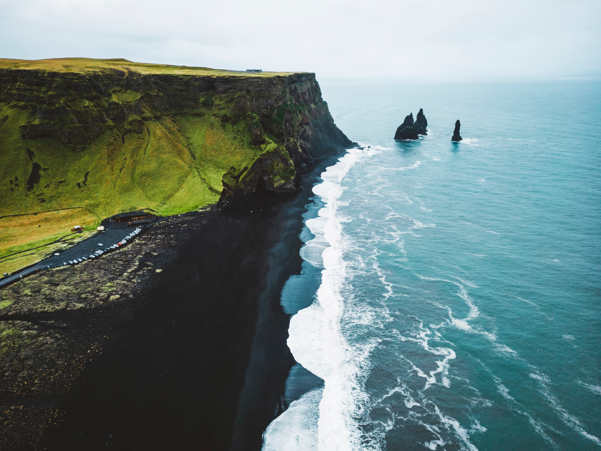 Golven breken langs de zwarte zandkust van Reynisfjara Beach in de buurt van Vik, IJsland, met uitzicht op de Reynisdrangar-rotsformaties.