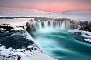 Icy winter view of Godafoss Waterfall with pastel pink skies seen during a private tour from Akureyri.