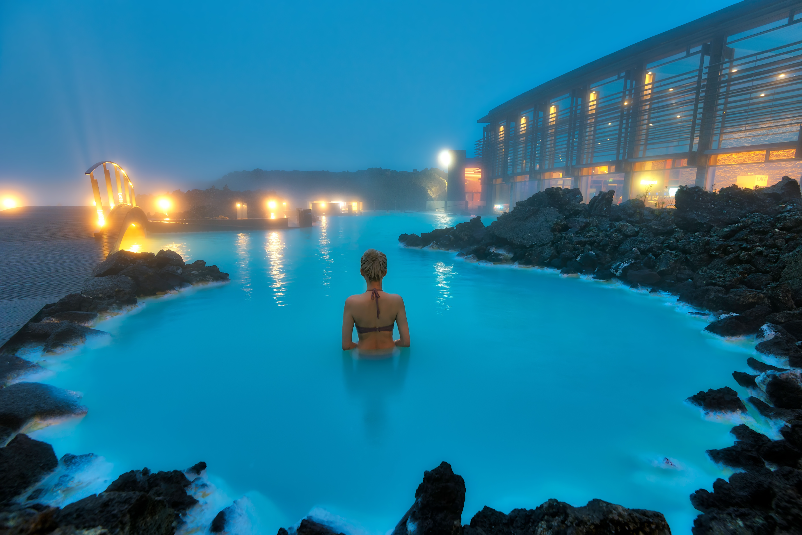 Une femme se baignant dans le Blue Lagoon, le célèbre spa géothermique islandais, entourée de roches volcaniques et d'un air hivernal brumeux.