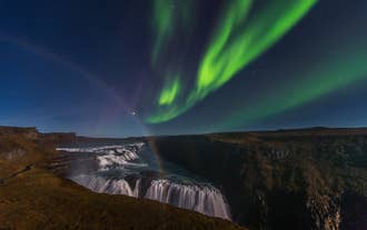 Les aurores boréales brillent au-dessus de la cascade de Gullfoss dans le Cercle d'or islandais, avec un arc-en-ciel dans la brume.